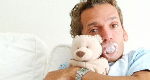 A man sucking a pacifier, wearing a bib, and holding a teddy bear