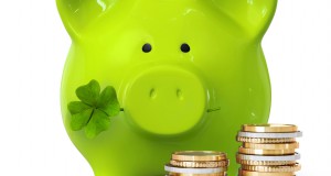Green piggy bank with clover and coin stacks