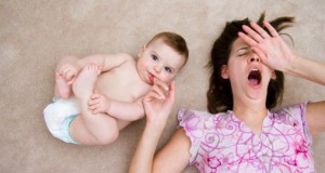 Mother yawns while baby sucks finger, laying down.