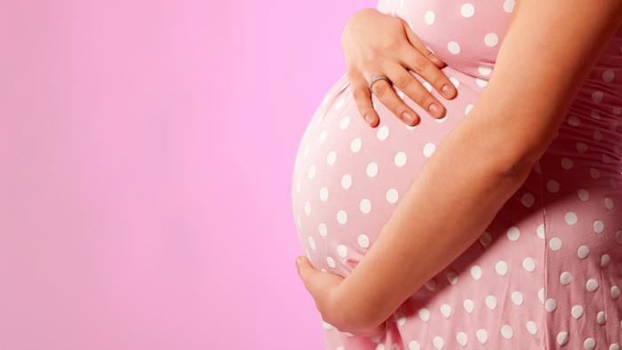Close-up of unrecognizable pregnant woman with hands over tummy at pink background; Shutterstock ID 160113932; PO: today.com
