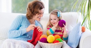 Mother and daughter knitting woolen scarf. Mom teaching child to knit. Crafts and hobby for parents and kids. Toddler girl kid with wool yarn in a basket. Knitted clothing for family with children.
