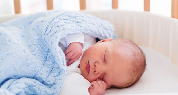 Newborn baby in hospital room. New born child in wooden co-sleeper crib. Infant sleeping in bedside bassinet. Safe co-sleeping in a bed side cot. Little boy taking a nap under knitted blanket.